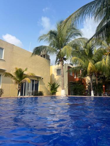 a swimming pool in front of a building with palm trees at CASA HUELLAS EN LA ARENA in Ixtapa