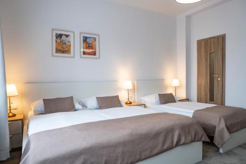 two beds in a white room with two lamps at Petit Dependance in Bratislava