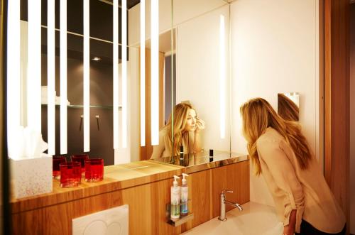 een vrouw die naar haar spiegelbeeld in de badkamer kijkt bij Alt Hotel Winnipeg in Winnipeg