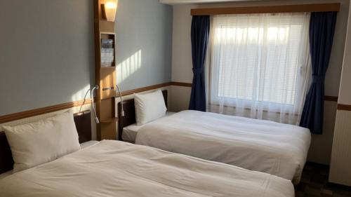 two beds in a hotel room with a window at Toyoko Inn Niigata Furumachi in Niigata