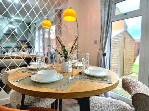 a wooden table with plates and glasses on it at The Charm Luxury House - 8mins to NEC, Birmingham Airport in Marston Green
