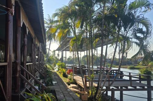 a building with palm trees next to a river at Nongsak Riverside Guesthouse & Nongsak Guesthouse in Ban Khon