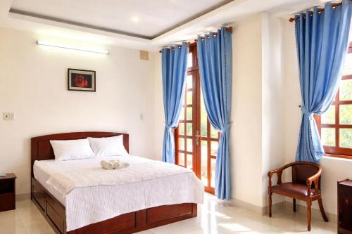 a bedroom with a bed with blue curtains and a chair at Green Ville Hotel Đồng Nai in Xa Dau Giay