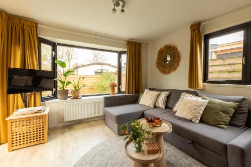 a living room with a gray couch and a tv at Loom - Modern Lodge in the Woods in Putten