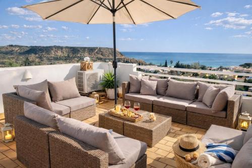 a patio with couches and an umbrella at Dreamy Sea View Apartment with Access to Private Pool & Stunning Rooftop in Luz