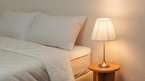 a bed with a white pillow and a table with a lamp at Gapyeong Nature Pension in Gapyeong