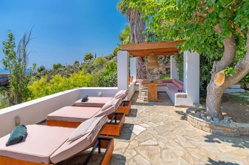 a patio with tables and benches and a tree at Villa Cleio where the sea meets absolute calm in Skiathos