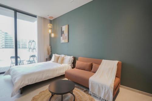 a bedroom with a bed and a couch and a window at Stylish modern studio near Miracle Garden with Gym, Pool and Padel court in Dubai