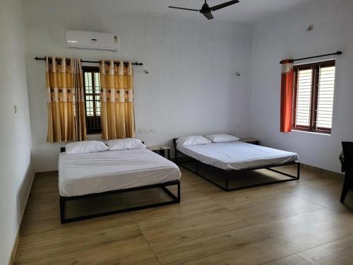 two beds in a room with two windows at Akalapuzha Homestay in Kozhikode