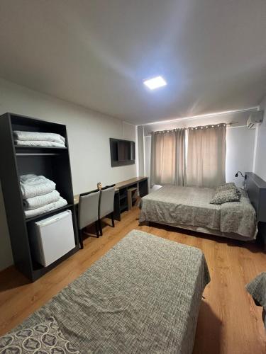 a bedroom with two beds and a desk and a tv at Hoteis Cattoni Executive in Lages