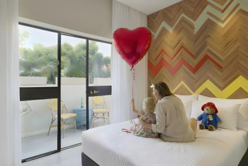 Eine Frau und ein Kind sitzen auf einem Bett mit einem roten Ballon in der Unterkunft Cucu Hotel in Tel Aviv