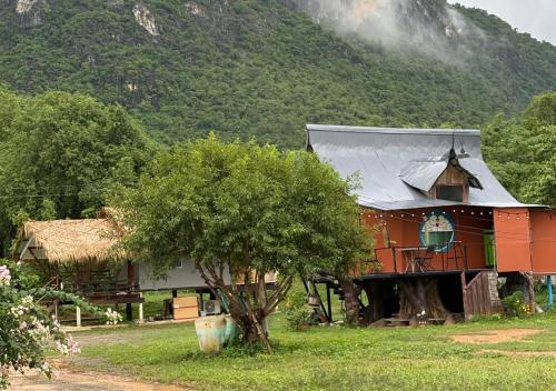 a red house with a grey roof in front of a mountain at ริมบึงโฮมสเตย์ in Ban Phu Noi