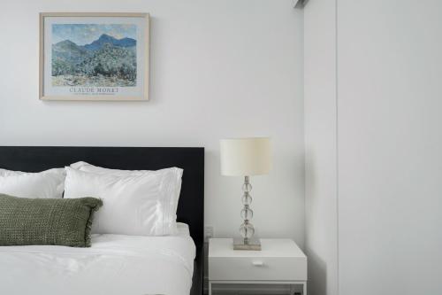 a bedroom with a white bed and a nightstand with a lamp at Modern 2 Bed Condo in the Junction+Parking in Toronto