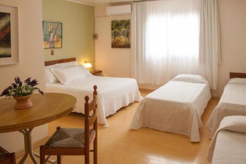 a bedroom with two beds and a table and a window at Hotel Primavera in Bento Gonçalves
