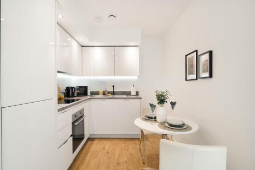 a kitchen with white cabinets and a small table at New-Build 1-Bed Apartment in Luton in Luton