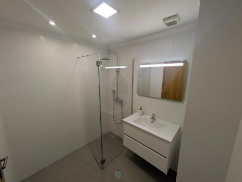 a bathroom with a shower and a sink and a mirror at Pátio do Garajau Apartamento T2 com estacionamento e varanda perto do Cristo Rei in Caniço