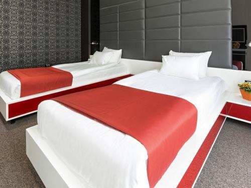 two beds with red and white sheets in a room at Nova City Garni Hotel Signature Collection in Belgrade