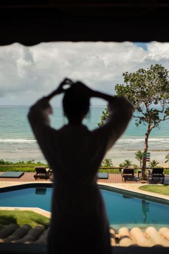 a man standing in front of a window looking at the ocean at Beijo do Vento Pousada in Arraial d'Ajuda