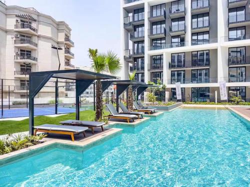 a swimming pool with lounge chairs in front of a building at Stylish modern studio near Miracle Garden with Gym, Pool and Padel court in Dubai