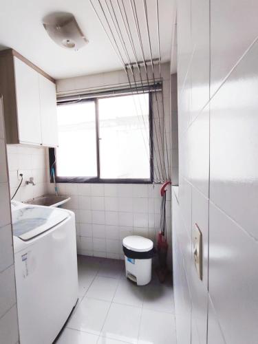 a white bathroom with a toilet and a window at Apartamento Completo I Suíte Casal in Guarapari