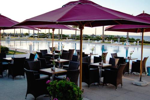 a group of tables with purple umbrellas in front of a pool at Amir Palace in Monastir