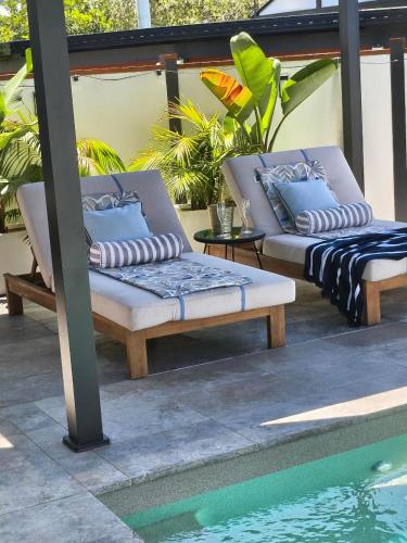 two lounge chairs with pillows sitting next to a pool at Ellie's Holiday Escape - Pool, Romantic, Fireplace in Coffs Harbour
