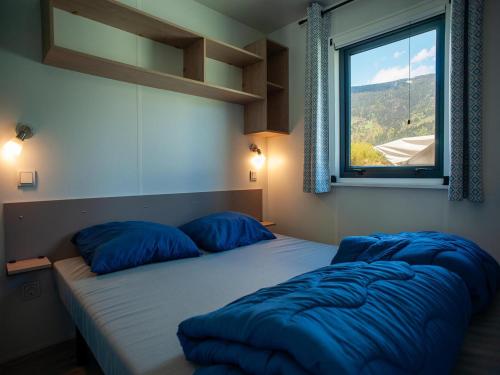 a bedroom with a bed with blue pillows and a window at Mobile Home in Austrian Countryside in Altossiach
