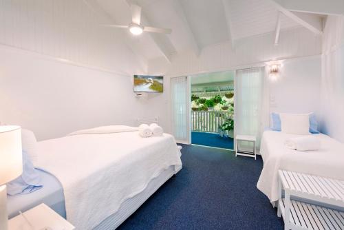a white bedroom with two beds and a balcony at Debbie's Place in Rainbow Beach