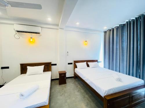 two beds in a room with blue curtains at Yehara Apartments in Weligama