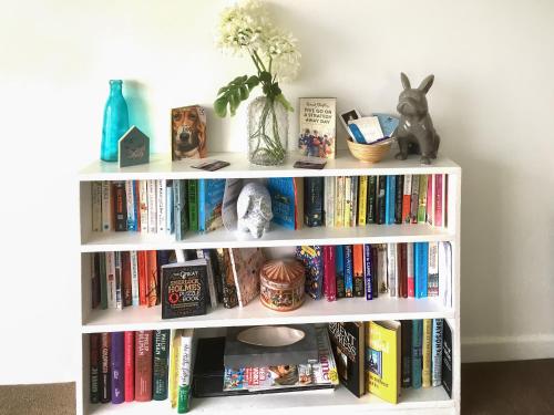 a white book shelf with books and a vase of flowers at The Hollies in Weston-super-Mare