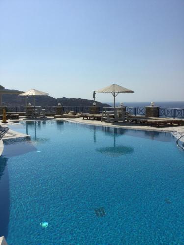 a large blue swimming pool with umbrellas and the ocean at Hermes-Ios Rooms To Let in Ios Chora