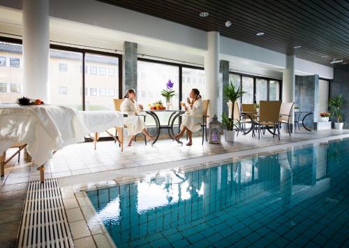 two women sitting at a table next to a swimming pool at Vinger Hotell in Kongsvinger