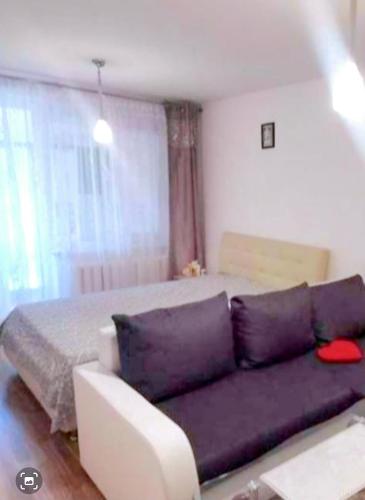 a living room with a purple couch in front of a bed at Butas Putinuose in Alytus