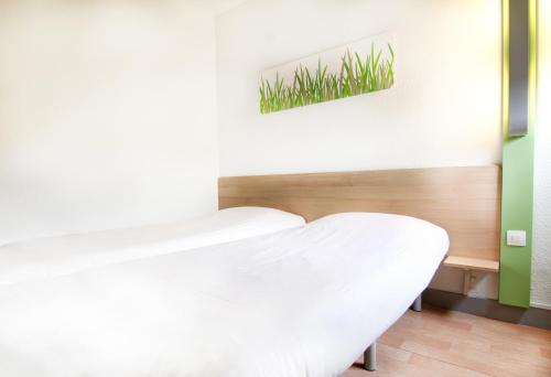 a bedroom with a white bed and a painting on the wall at ibis budget Besançon Ecole Valentin in Besançon