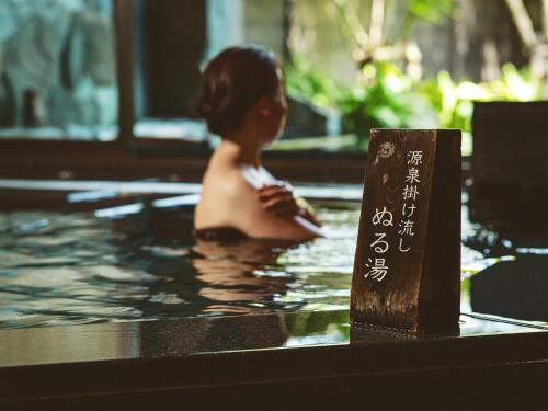a woman in a swimming pool with a sign in the water at Etajimasou Hotel & SPA Hiroshima in Etajima
