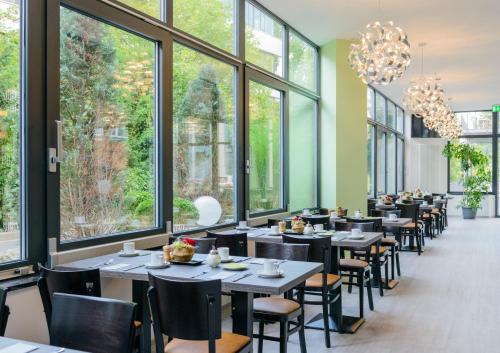 a dining room with tables and chairs and large windows at Novina Hotel Wöhrdersee Nürnberg City in Nürnberg