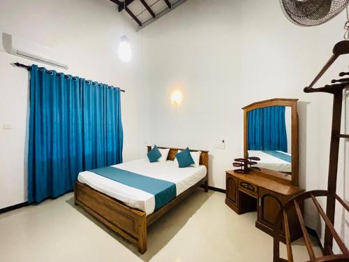 a bedroom with a bed with blue curtains and a mirror at Sasanda Villa in Weligama