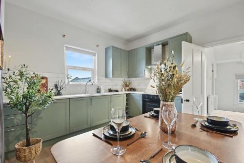 a kitchen with green cabinets and a wooden table with wine glasses at Maple Snug- Wyndale Signature Stays in Great Malvern