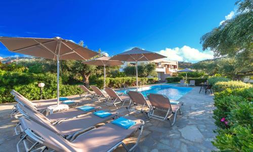 a group of chairs and umbrellas next to a pool at Plaisir Beachside Apts in Agios Nikolaos