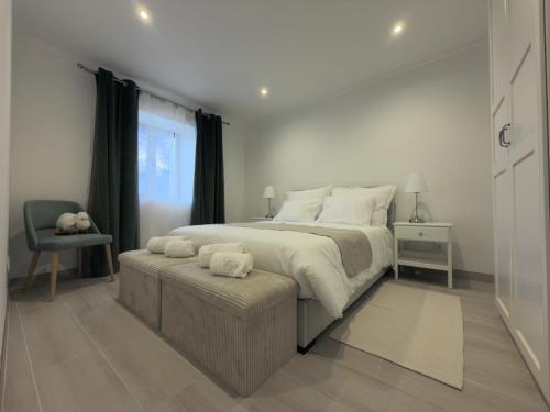 a white bedroom with a large bed and a chair at Casinhas do Penedo in Canelas