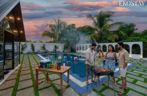 a group of three people standing next to a swimming pool at EKOSTAY - Oakwood Chalet in Alibaug