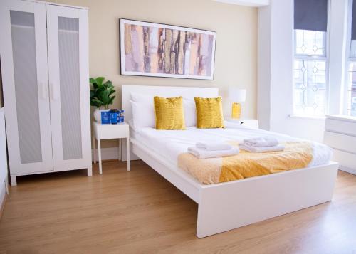 a white bedroom with a white bed with yellow pillows at CONTRACTOR READY - spacious and bright 5 bed house! in Luton