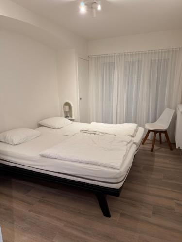a white bedroom with a large bed and a chair at De Haan App 1 in De Haan