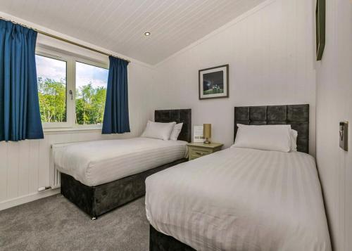 two beds in a bedroom with blue curtains at Finest Retreats - Silverwood Junior Chalet in Errol