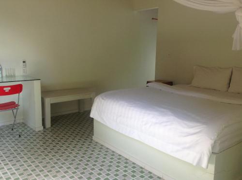 a bedroom with a white bed and a red chair at Maison de l'Amant in Cai Be