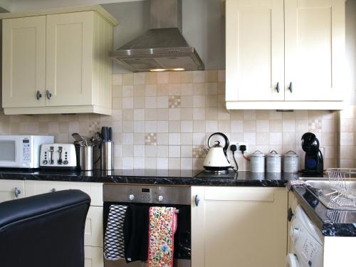 a kitchen with white cabinets and a tea kettle on the stove at Willow Cottage in Bentley