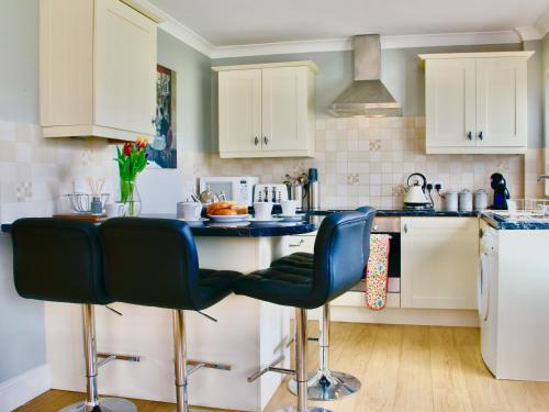 a kitchen with white cabinets and blue bar stools at Willow Cottage in Bentley