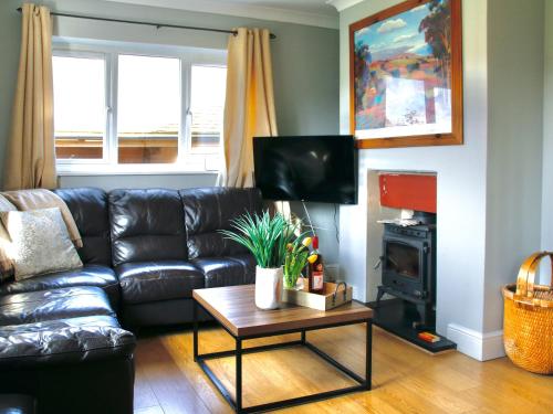 a living room with a black leather couch and a table at Willow Cottage in Bentley