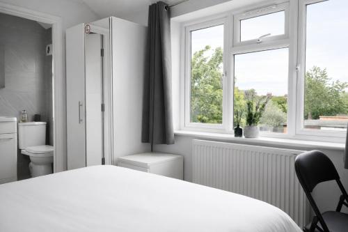 a white bedroom with a bed and two windows at Walton Suites in Watford