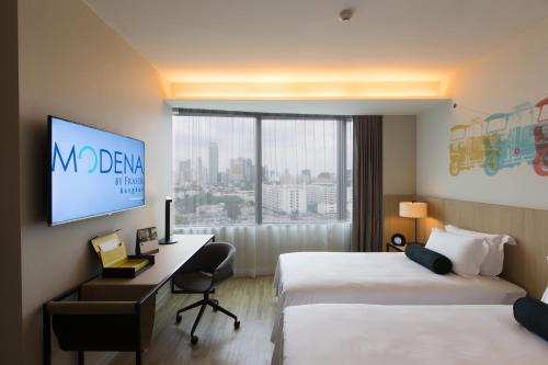 a hotel room with two beds and a desk and a tv at Modena by Fraser Bangkok in Bangkok